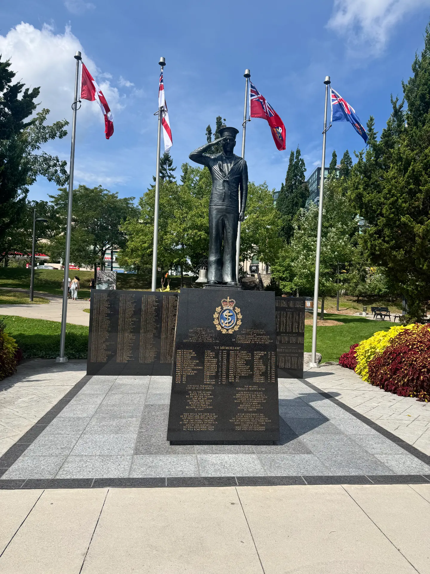 Bronze saluting sailor statue standing above granite memorial walls with four flags flying behind